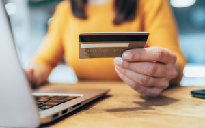 A person sitting at a laptop holding a credit card