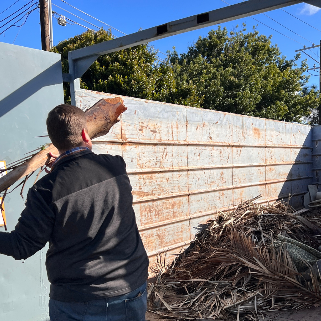 Man tosses a log in a oversized dumpster