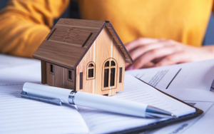 A picture of a small wooden house replica over an open notebook in the foreground, a person