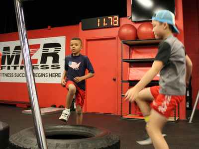 Two young athletes doing high knees on a tire at MZR Fitness' Strength and Conditioning class