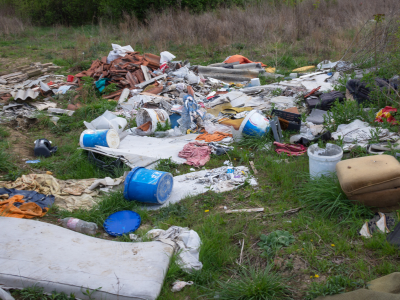 A picture of trash litter including a mattress and ottoman all over a patch of grass