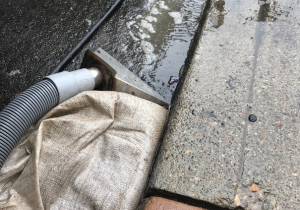 Vacuum in front of sandbag in gutter, collecting wash water