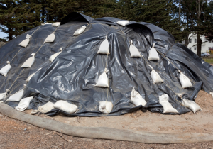 Dirt pile covered with a tarp and sandbags on top, surrounded by straw wattle