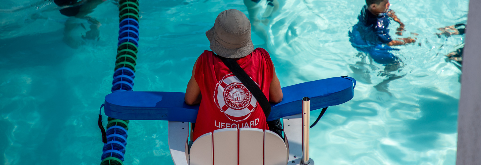 An image of a lifeguard guiding a child in the pool with a floatation device during swim lessons at the SLO Swim Center.