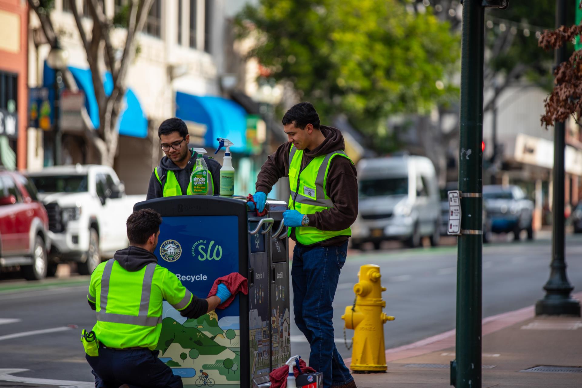 Three volunteers clean the Sustainable SLO waste and recycling bins.