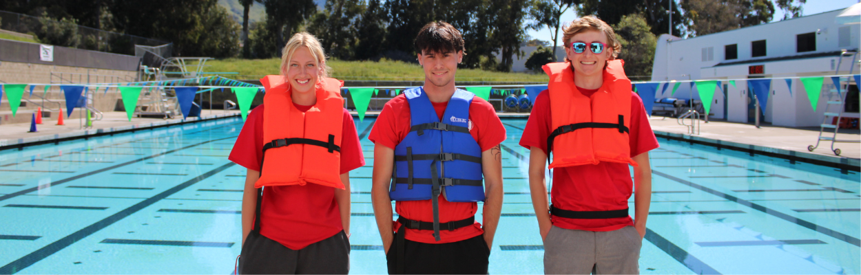 A picture of 3 SLO Swim Center lifeguards wearing life jackets standing in front of the pool.