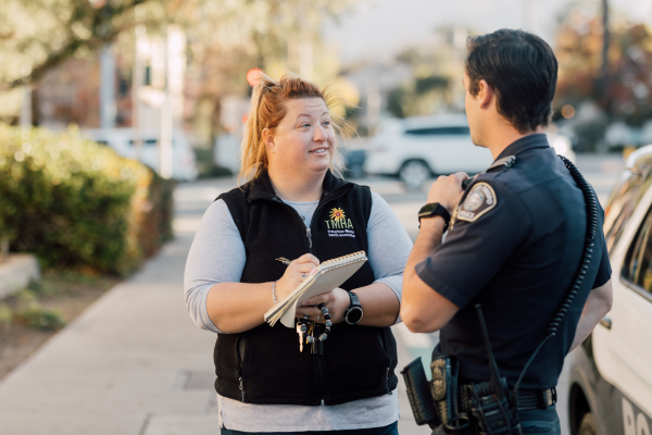 The Community Action Team stands on a sidewalk near a police vehicle.